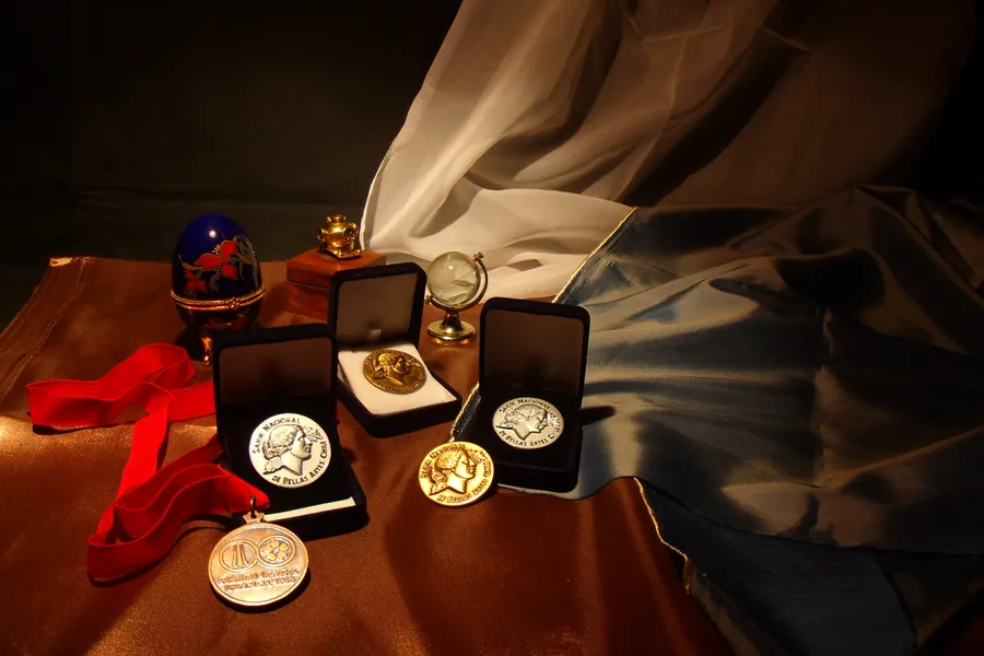 Medallas de salón en sus estuches de terciopelo, sobre una tela dorada, junto a una cinta roja y un pequeño globo terráqueo de cristal.