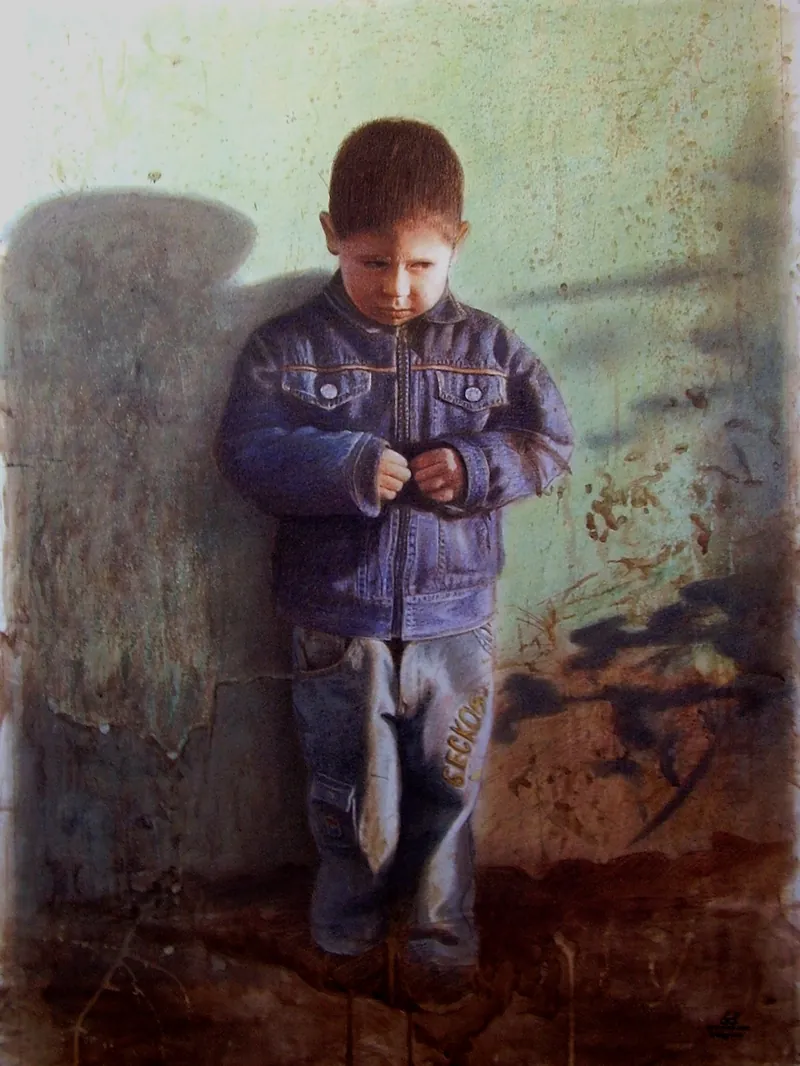 Niño con chaqueta de mezclilla de pie junto a un muro, mirando hacia abajo.
