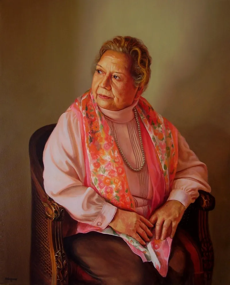 Retrato de una señora mayor sentada en un sillón, con pañuelo rosado y collar de perlas.